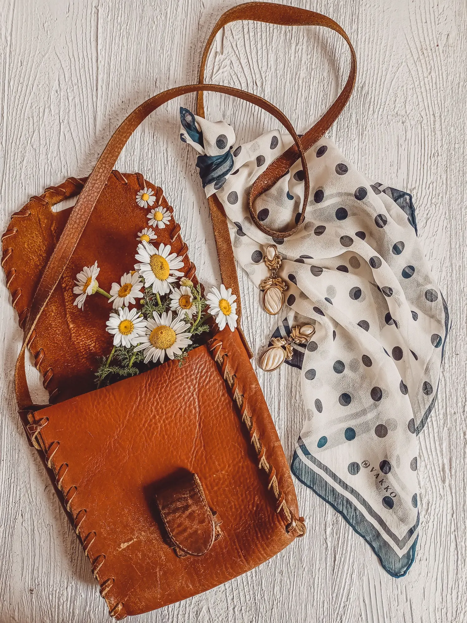 A worn leather shoulder bag styled with a silk scarf and fresh daisies