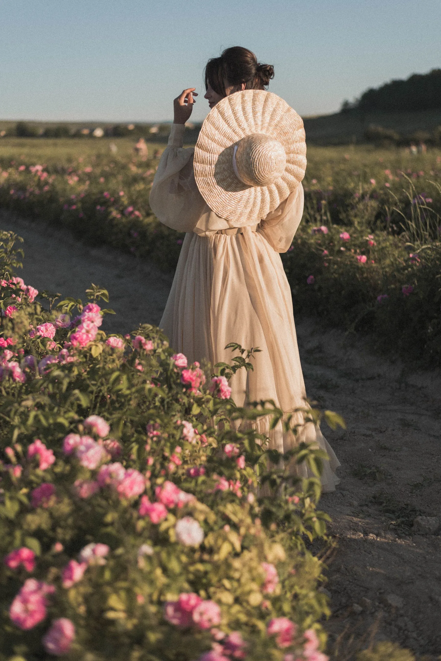 Woman walking through a garden in a long vintage dress and straw hat